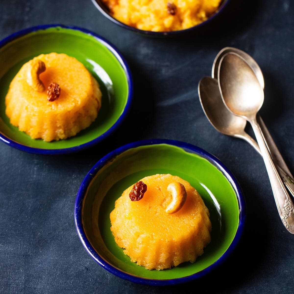 kesari recipe served in three green plates with brass spoons by the side.