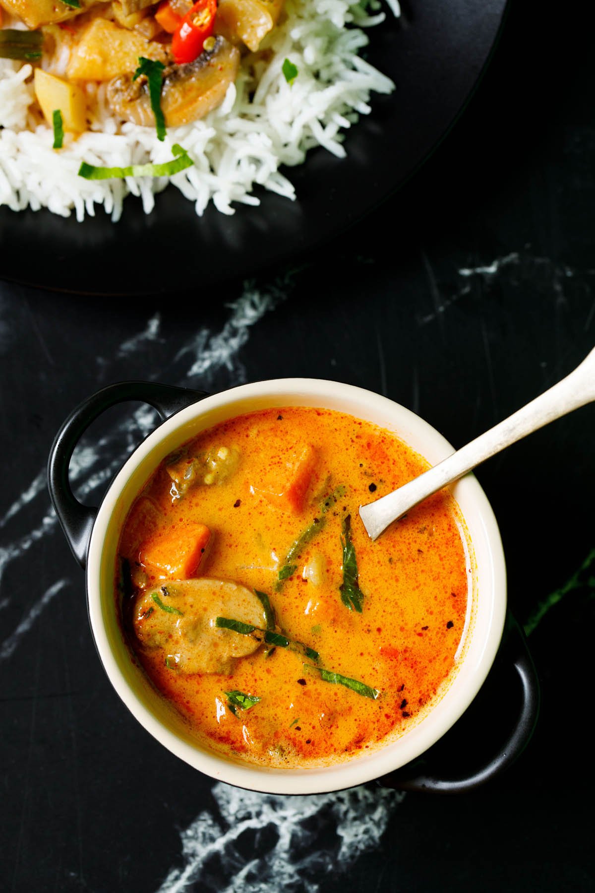 red thai curry filled in a cream bowl with a spoon inside on a black marble table