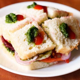 bombay veg sandwich dotted with green chutney and tomato ketchup on a white plate.