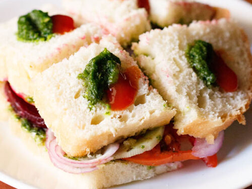 bombay veg sandwich dotted with green chutney and tomato ketchup on a white plate.