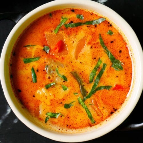 thai curry garnished with basil chiffonade in a cream ceramic bowl on a black marble table