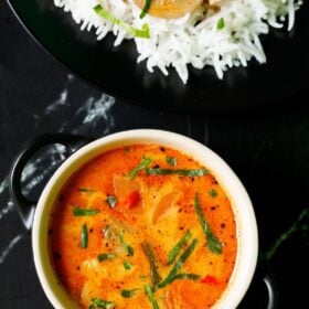 overhead shot of thai curry filled in a cream bowl with a black plate of rice and curry on top on black marble table