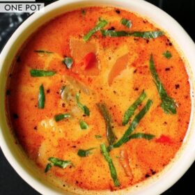 overhead shot of thai red curry garnished with basil chiffonade in a cream ceramic bowl on a black marble table with text layovers