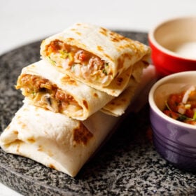 burrito with filling seen on granite board with bowls of sour cream and pico de gallo at the side