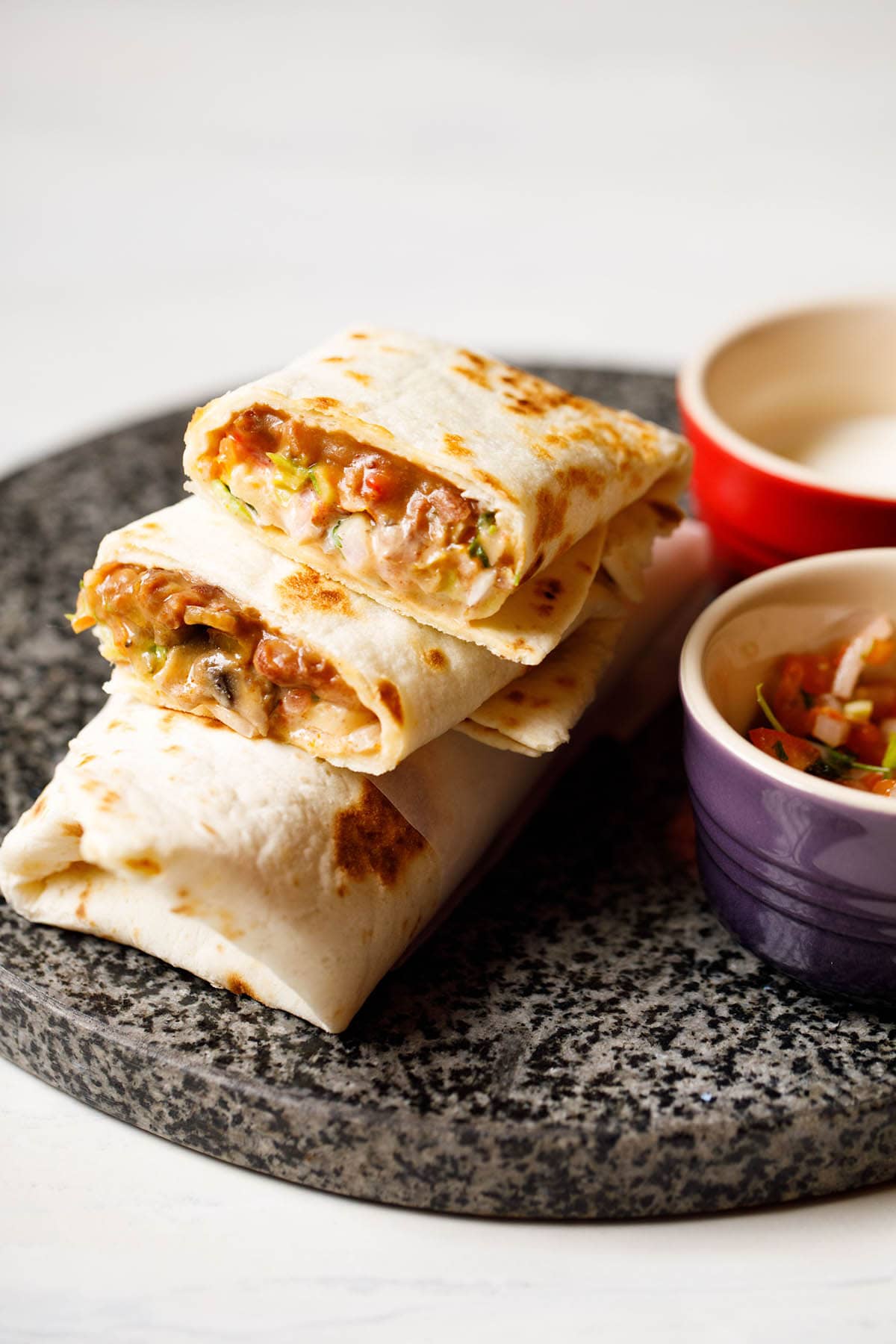 burrito with filling seen on granite board with bowls of sour cream and pico de gallo at the side