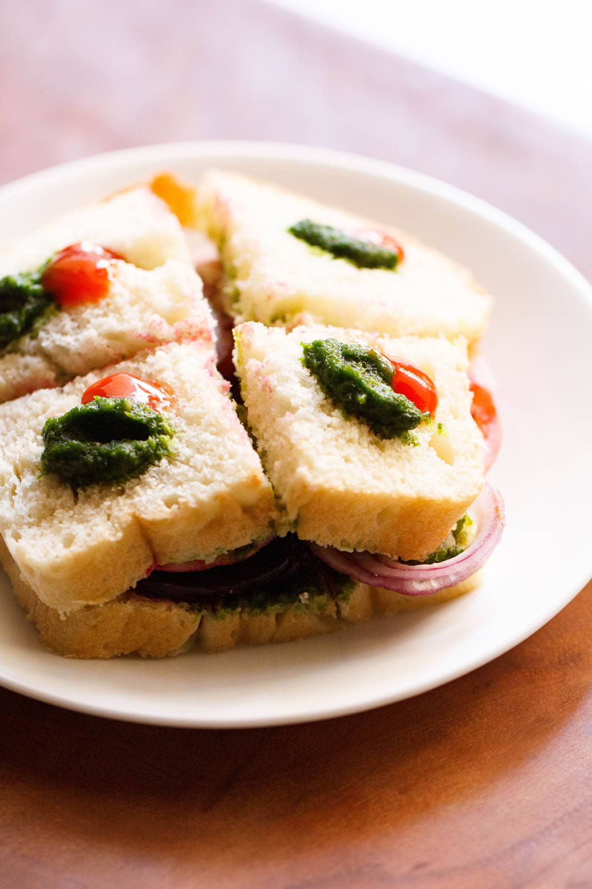 veg sandwich dotted with green sauce and ketchup, served on a white plate. 