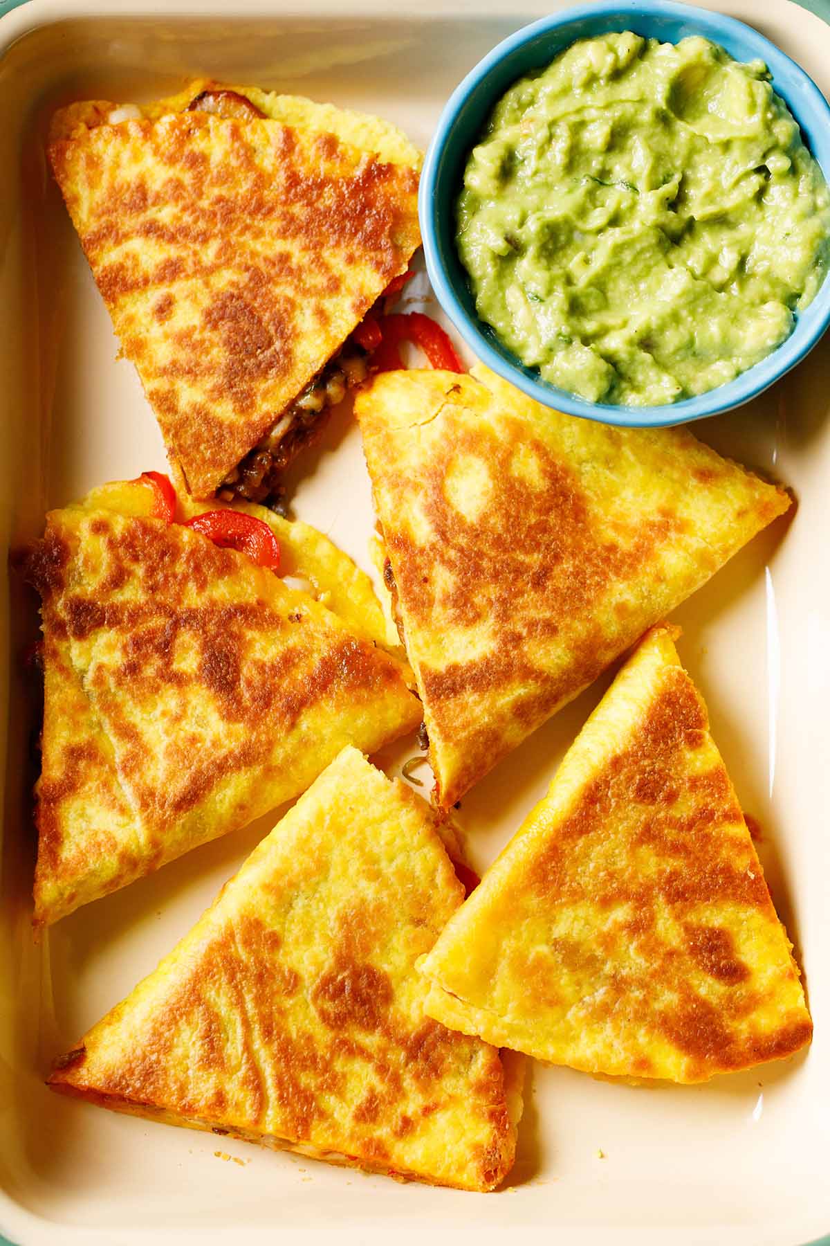 quesadilla triangles served in a tray with a side of guacamole in a blue bowl.