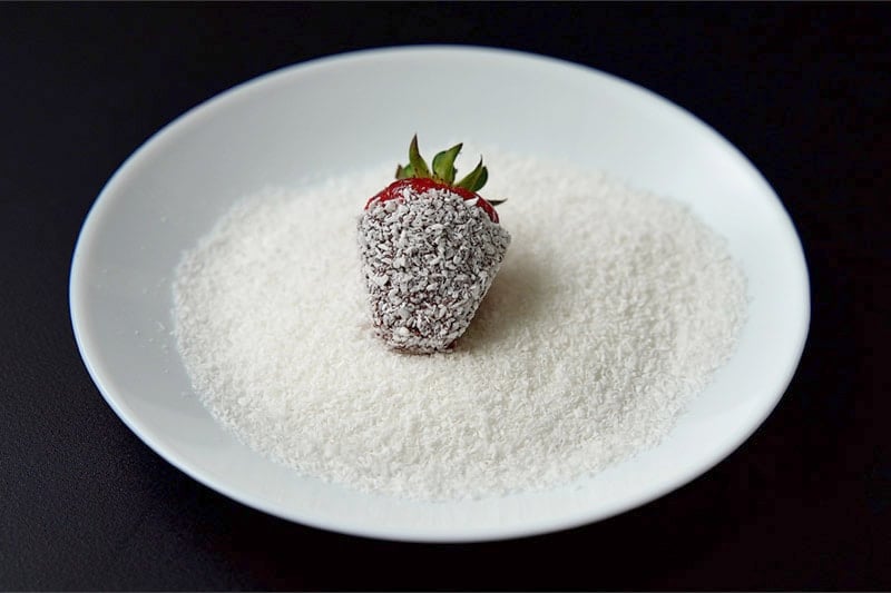 rolling chocolate dipped strawberry in dessicated coconut