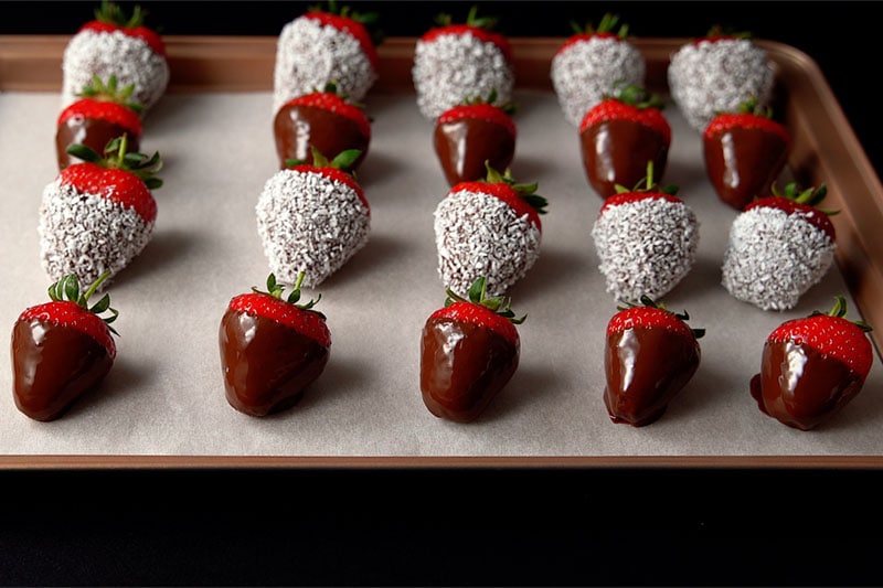 4 rows of chocolate dipped strawberries on a parchment lined tray with alternating plain and coconut 