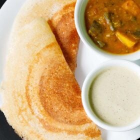 two folded, golden, crisp placed next to white bowls filled with sambar and coconut chutney on a white plate