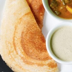 overhead shot of two folded dosa with bowls filled with sambar and coconut chutney on a white plate with text layovers