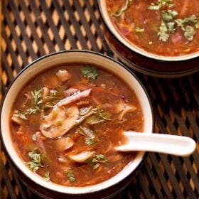 hot and sour soup with coriander garnish in a soup bowl with a white spoon inside on a dark brown bamboo tray