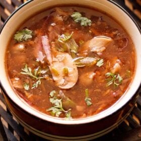 closeup shot of hot and sour soup in a black rimmed bowl on a dark brown bamboo tray.