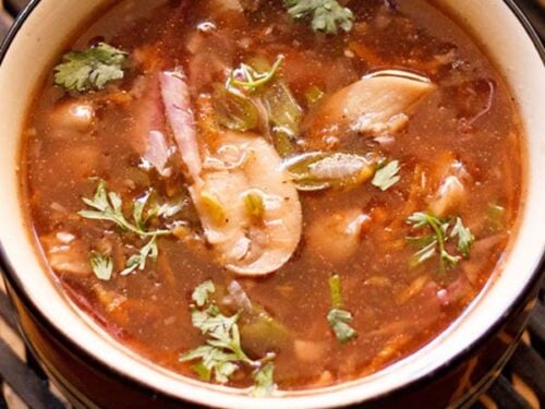 closeup shot of hot and sour soup in a black rimmed bowl on a dark brown bamboo tray.