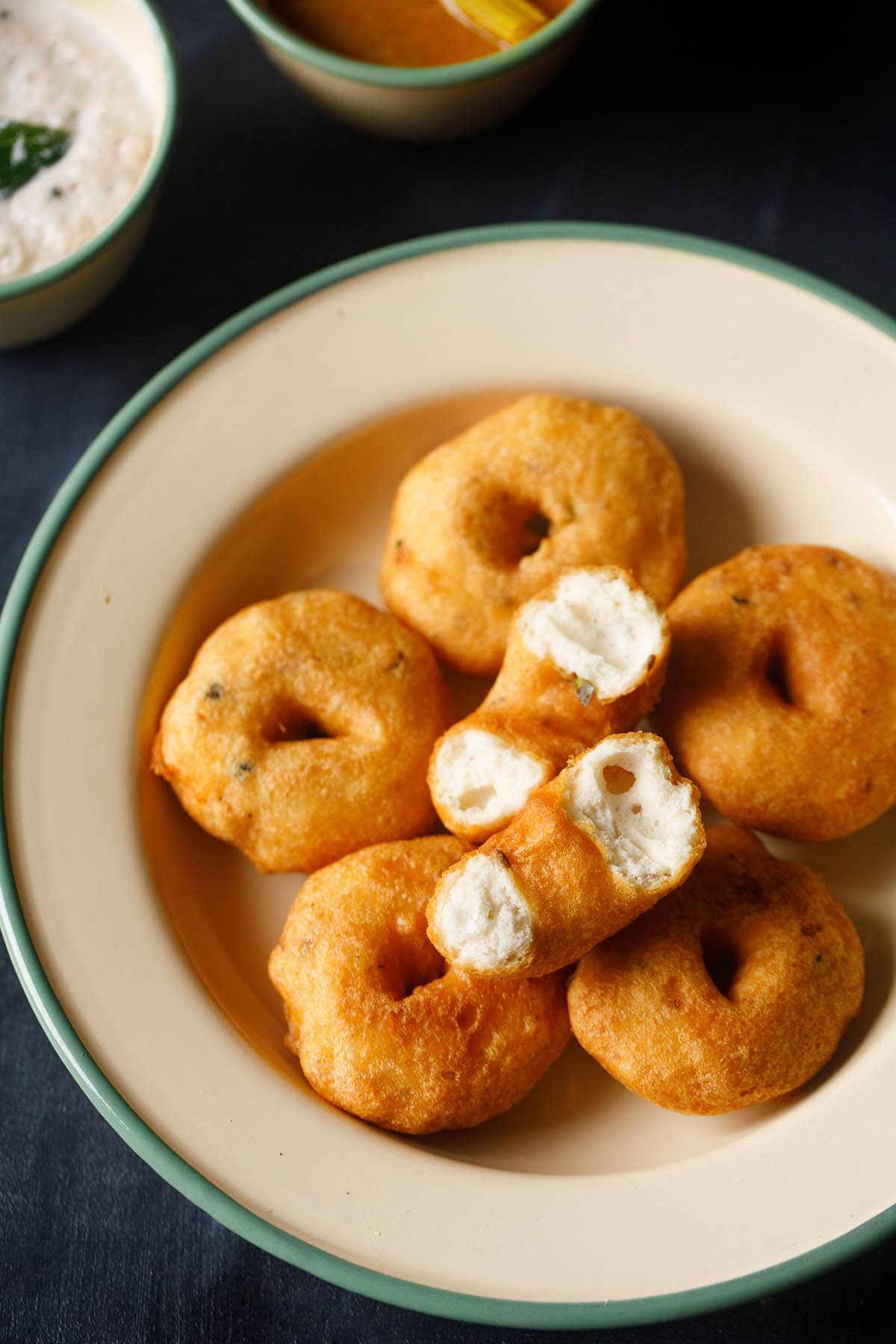 two halves of medu vada showing the fluffy texture placed on a layer of neatly stacked 5 vada in a cream colored shallow plate