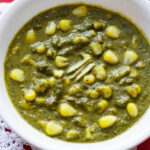 closeup shot of palak corn in a white bowl with three ginger juliennes on a white doily placed above folded red napkin