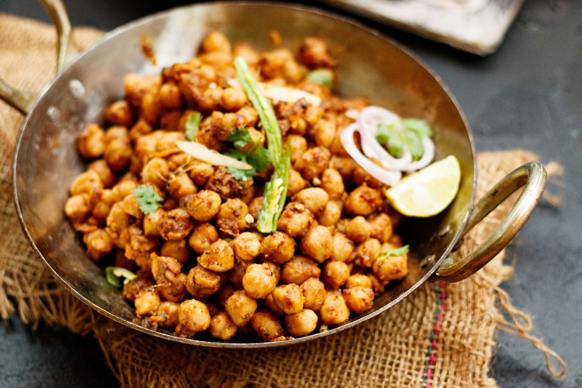 pindi chana served in a metal kadai (wok) with green chili strips, sliced onions and lemon wedge