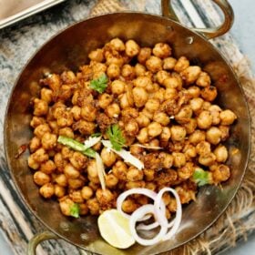 overhead shot of pindi chana in a metallic wok garnished with onion slices, cilantro, lemon wedge and green chilli strips