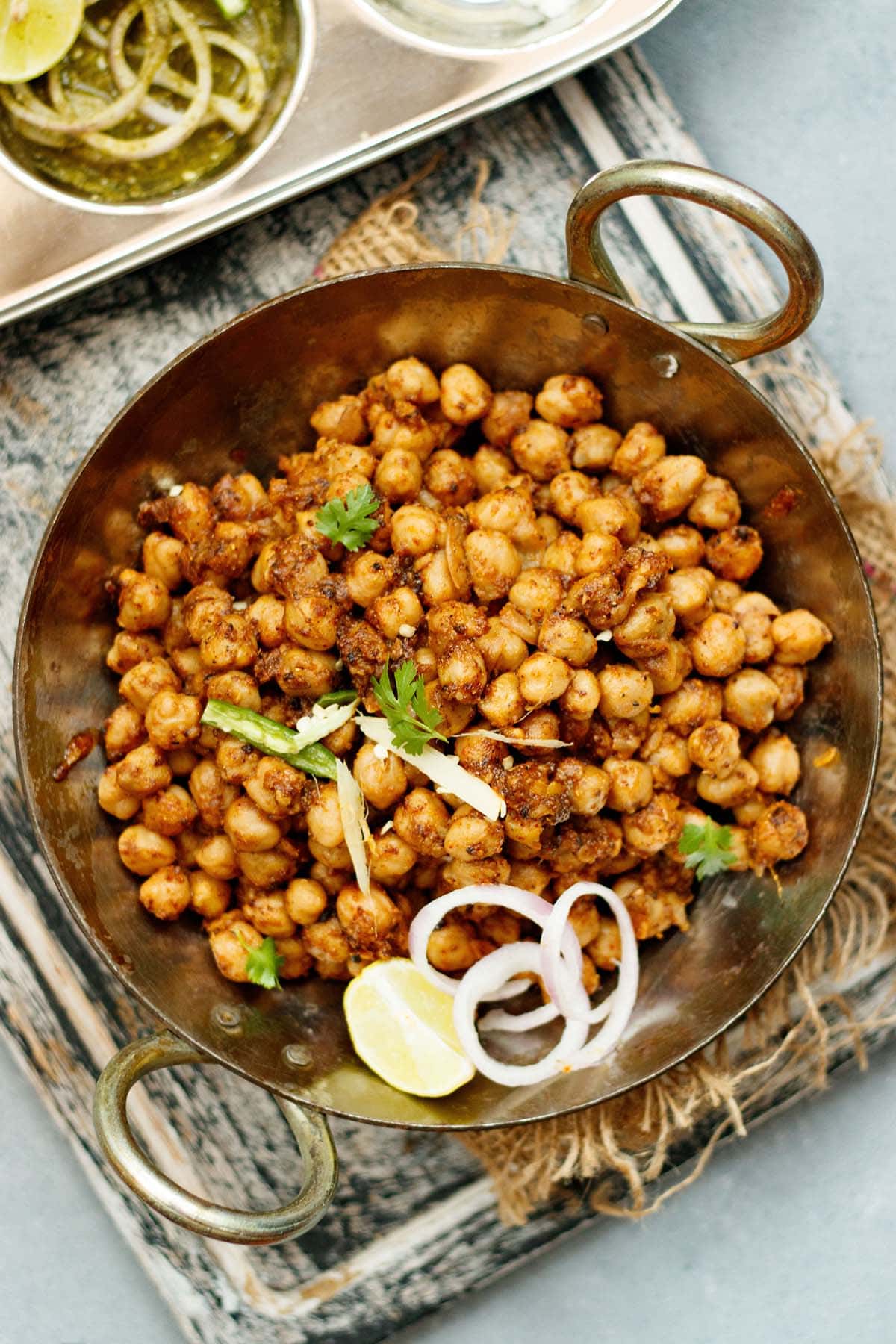 overhead shot of pindi chana in a metallic wok garnished with onion slices, cilantro, lemon wedge and green chilli strips