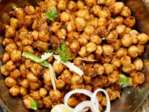 closeup shot of pindi chana in a metallic wok garnished with onion slices, cilantro, lemon wedge and green chilli strips