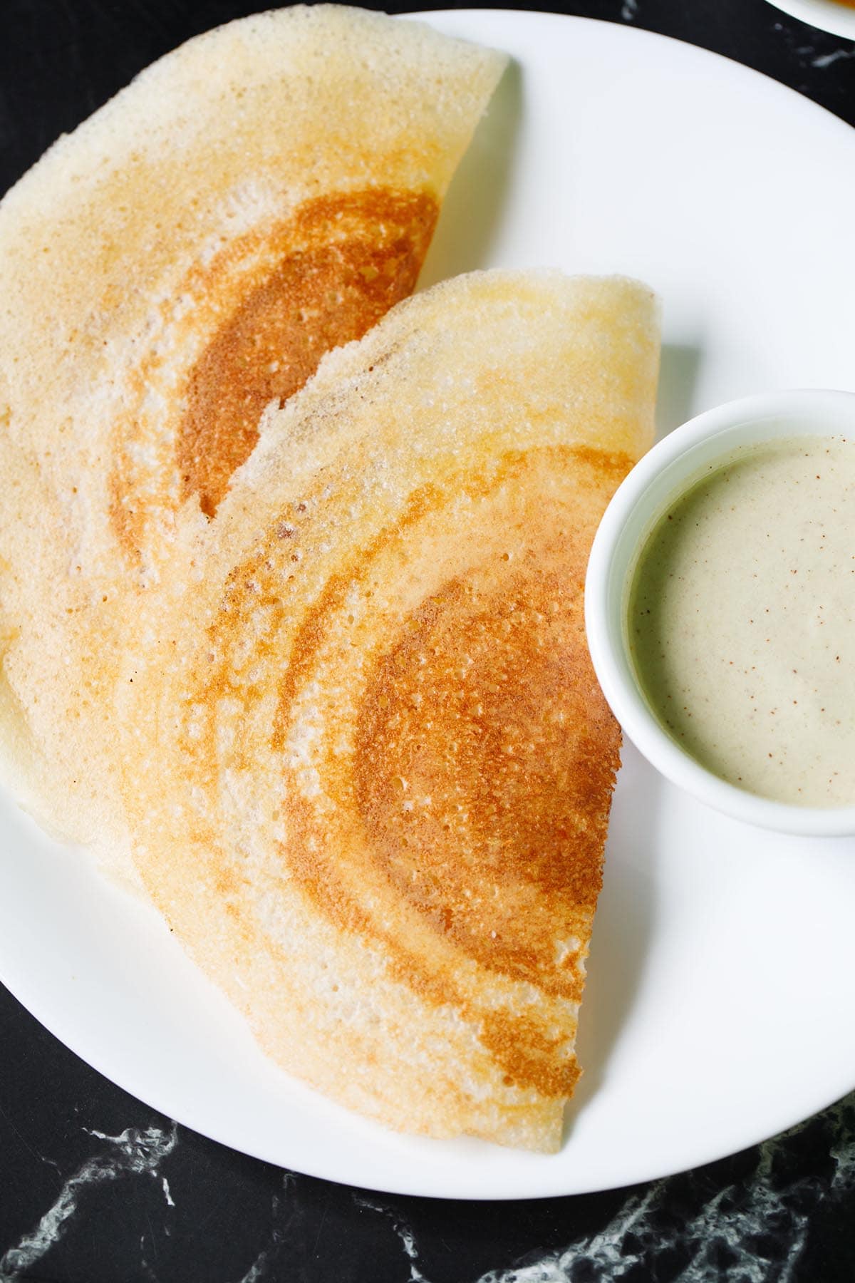 close up shot of crisp sada dosa folded next to a bowl of coconut chutney on a white plate