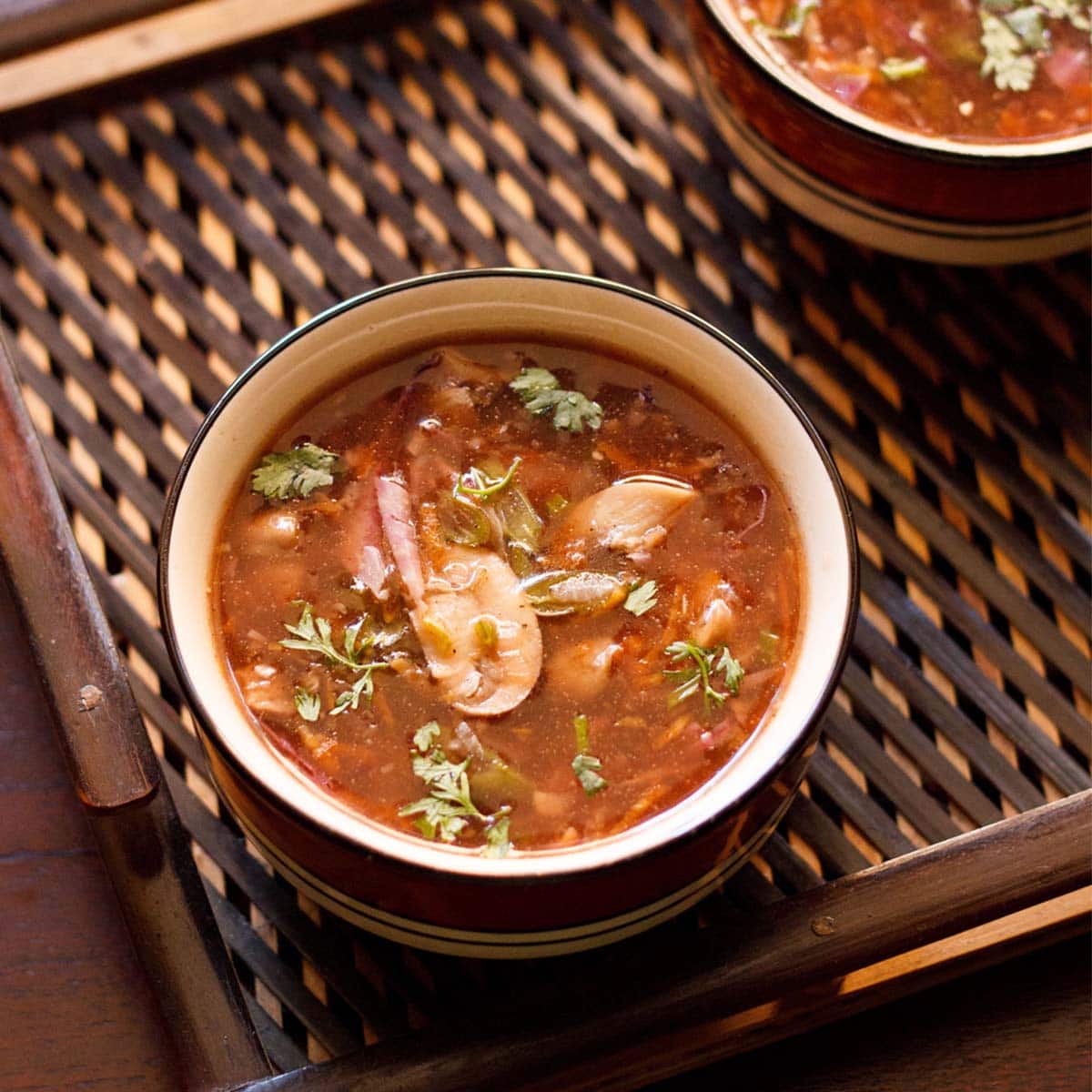 veg hot and sour soup in a black rimmed bowl or a dark brown bamboo tray
