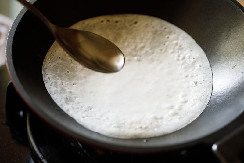 using a spoon to drizzle in some oil while appam cooks
