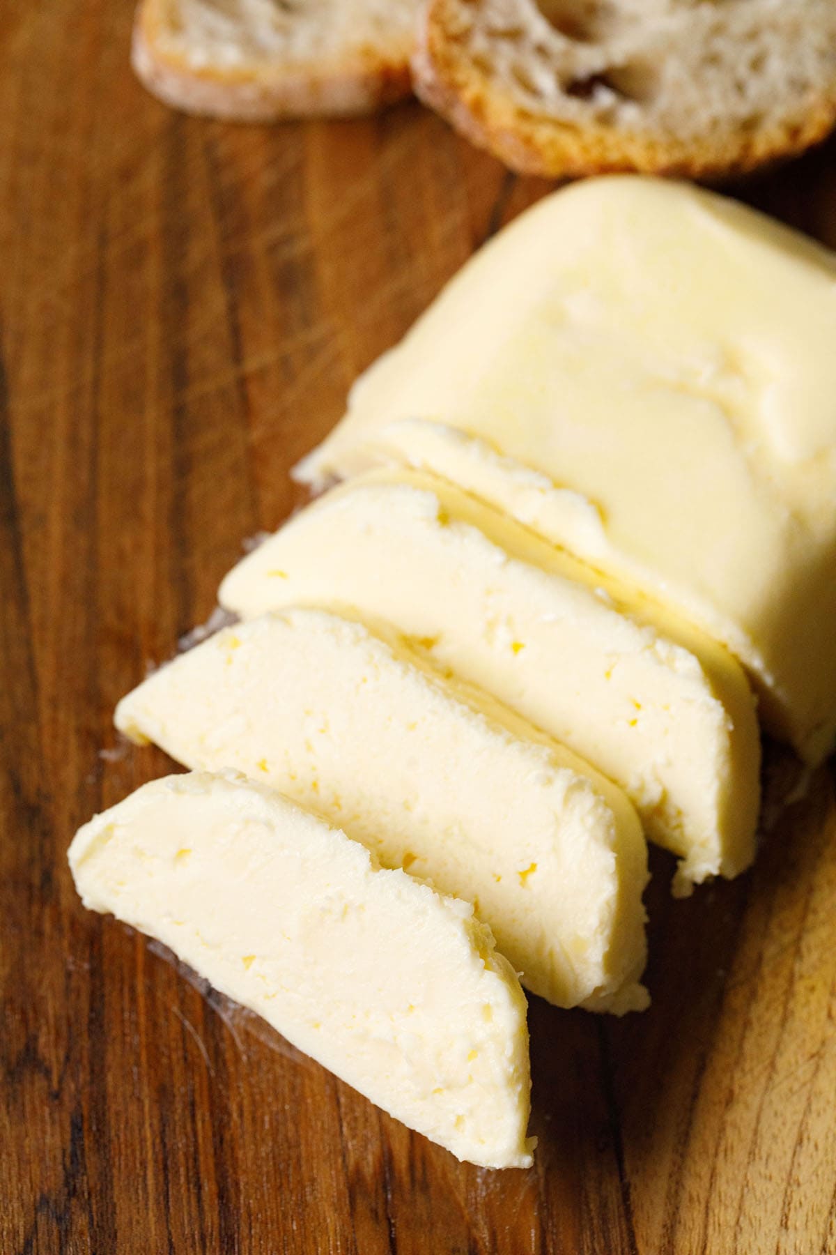 block of butter cut in three thick sliced on a wooden brown board