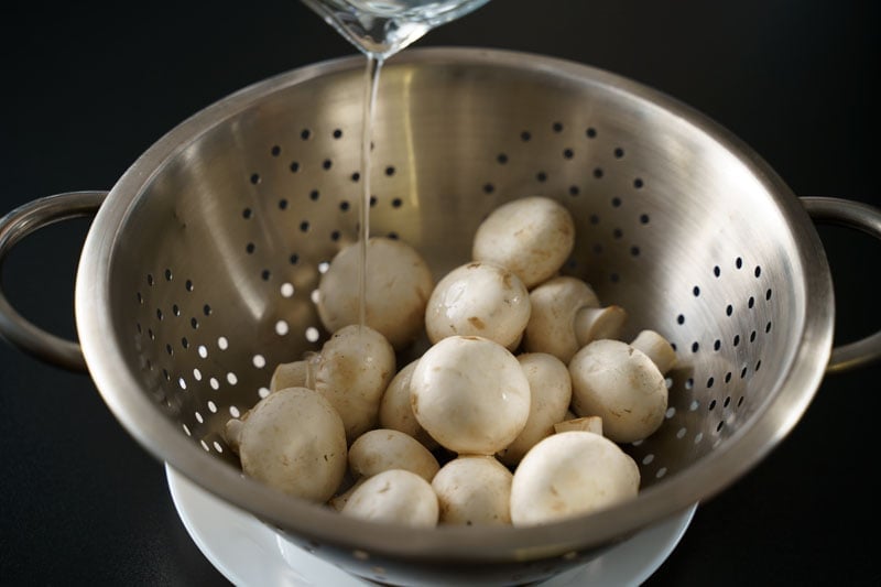 mushrooms being rinsed with water in a colander