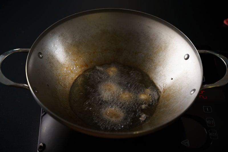 batter coated mushrooms being shallow fried in oil in wok