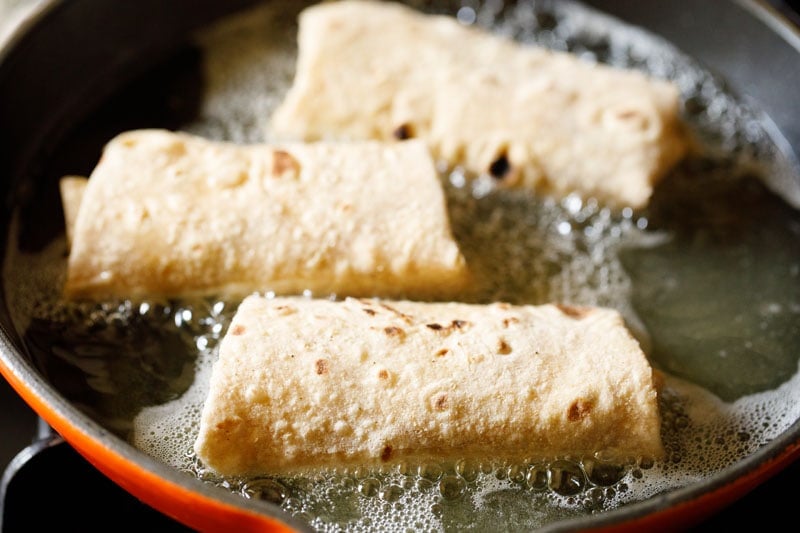 three chimichangas frying in oil