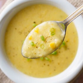 sweet corn soup in a silver spoon on top of white bowl filled with the soup.