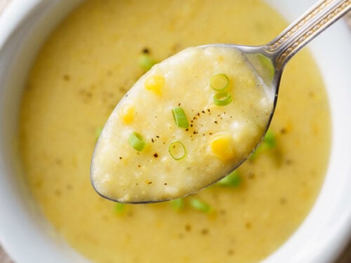 sweet corn soup in a silver spoon on top of white bowl filled with the soup.