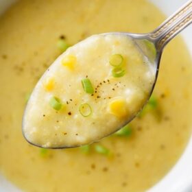 sweet corn soup in a silver spoon on top of white bowl filled with the soup.