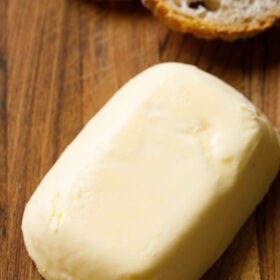 block of homemade butter on brown wooden board with baguette slices on top