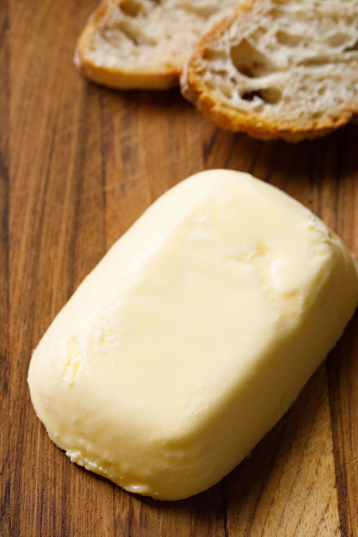 block of homemade butter on brown wooden board with baguette slices on top