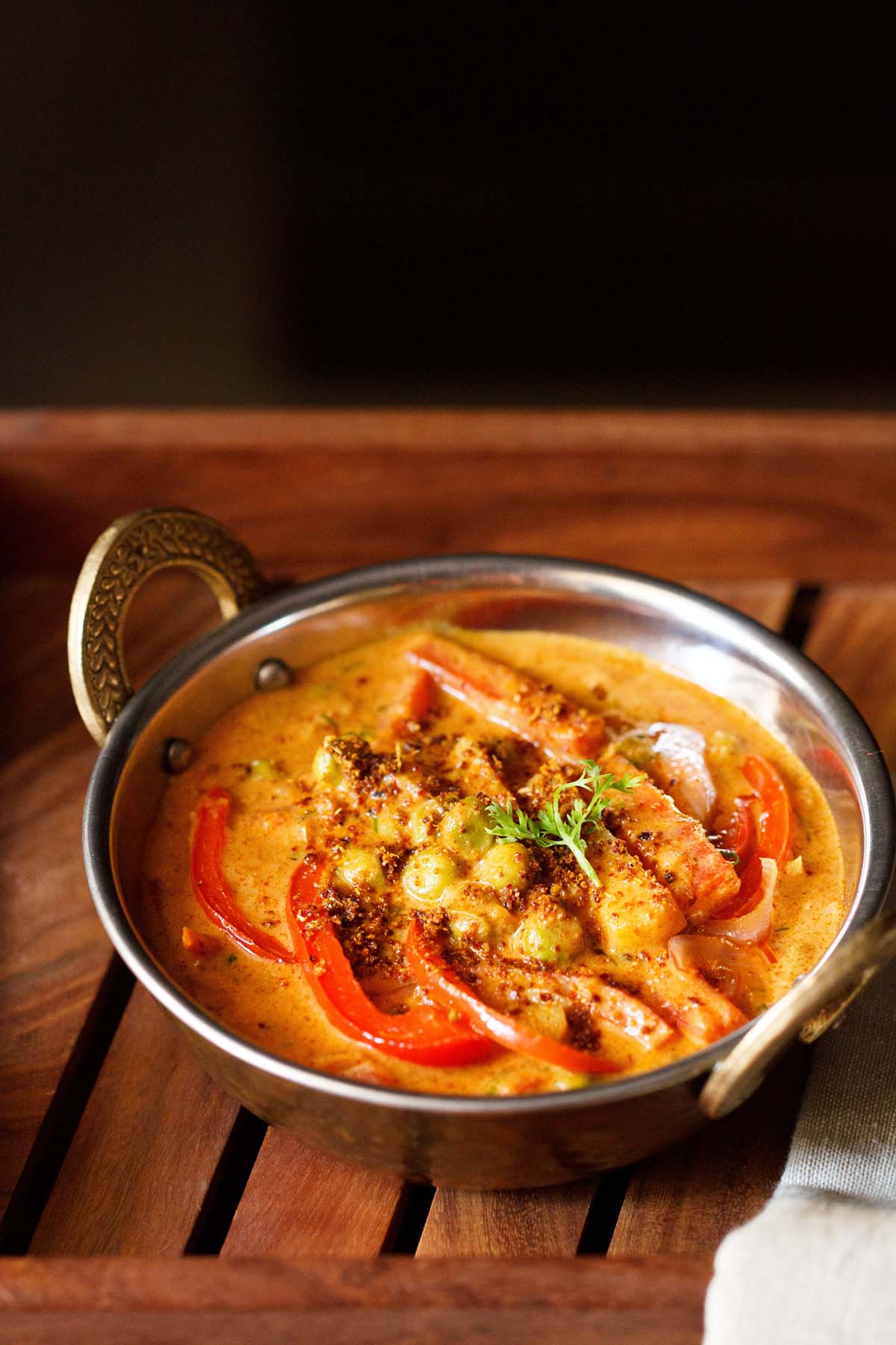 kadai vegetable in a metal kadai with a sprig of coriander and three red bell pepper slices as garnish