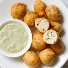 overhead shot of white plate having halved mysore bonda showing the fluffy texture on top of remaining bonda next to a side of light green coconut chutney