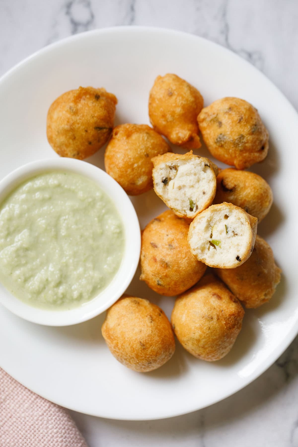 overhead shot of white plate having halved mysore bonda showing the fluffy texture on top of remaining bonda next to a side of light green coconut chutney