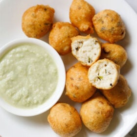 overhead shot of white plate having halved mysore bonda showing the fluffy texture on top of remaining bonda next to a side of light green coconut chutney