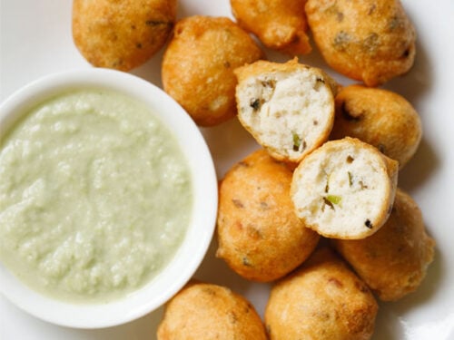 overhead shot of white plate having halved mysore bonda showing the fluffy texture on top of remaining bonda next to a side of light green coconut chutney