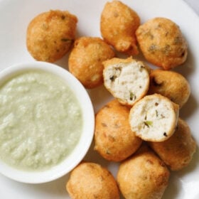 overhead shot of white plate having halved mysore bonda showing the fluffy texture on top of remaining bonda next to a side of light green coconut chutney with text layovers