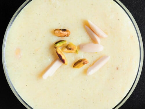 closeup overhead shot of phirni with pistachios and almond slivers garnish on glass bowl on black board