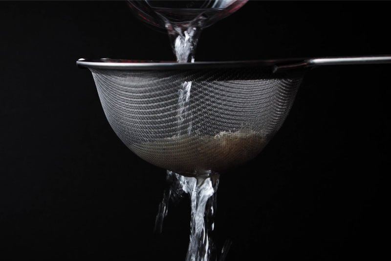 rice being rinsed in strainer with water pouring from top