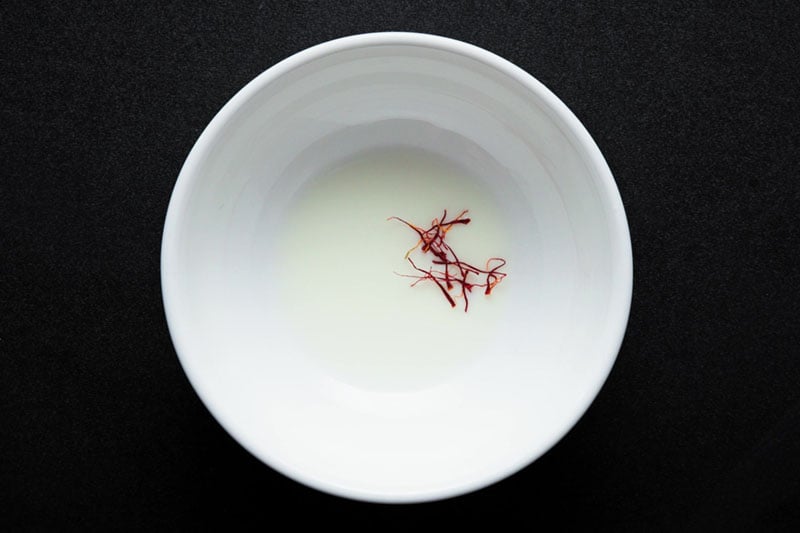 overhead shot of milk and saffron strands in a small white bowl