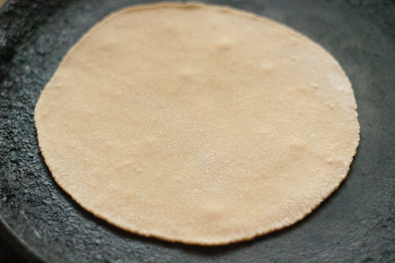 raw round of dough added to hot tawa, with small bubbles beginning to appear