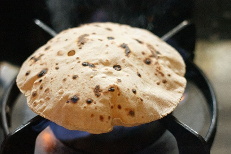 puffed up soft roti after flipping on the direct flame shows some dark blistered spots from the flame