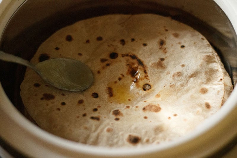 cooked phulkas in a roti basket being brushed with ghee to keep them soft