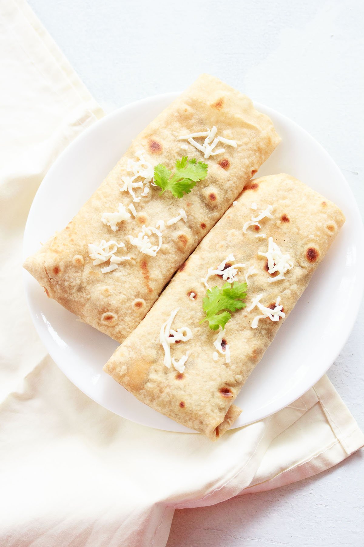 overheat shot of spinach rolls on a white plate topped with some grated cheese and two sprigs of cilantro