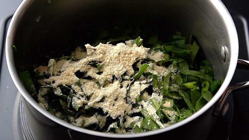 adding gram flour to spinach in pan